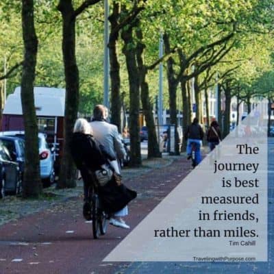 Photo of an elderly man and woman riding on a single bicycle on a tree-lined sidewalk in Amsterdam. Text shows a travel quote - "The Journey is best measured in friends rather that miles."