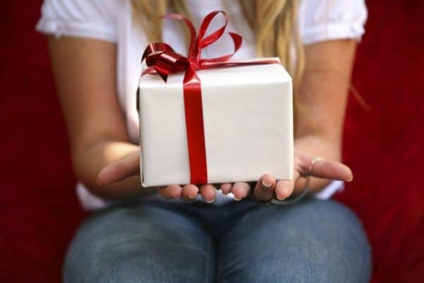 Woman holding present in white wrapping paper and red ribbon - The Gift of Gratitude