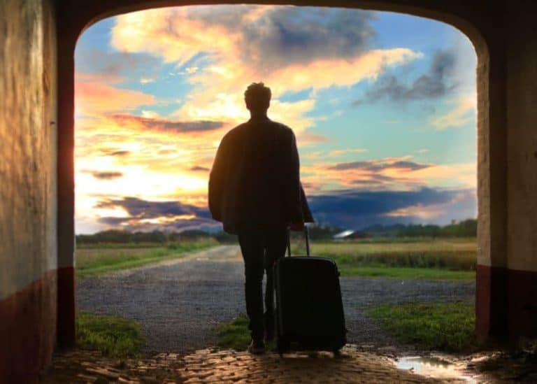 Silhouette of man with suitcase, walking toward the sunset