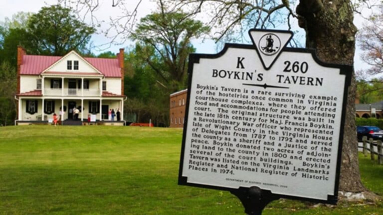 A historical marker sign stands in front of Boykins Tavern with a summary of its history. This 2-story historic home and gathering place was built in the late 18th century in Virginia.