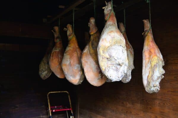 Seven large hams hang curing in a smoker building in Virginia.