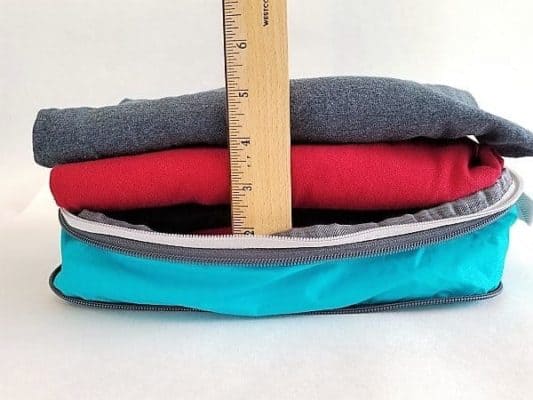 An open unzipped Compression Packing Cube with 5 T-shirts inside and a ruler showing how tall the pile of clothes is.