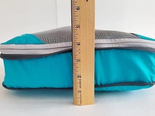 An aqua Gorex Packing Cube with one zipper closed. It contains 5 T-shirts. A ruler next to the cube shows how much space it takes up before compressed.