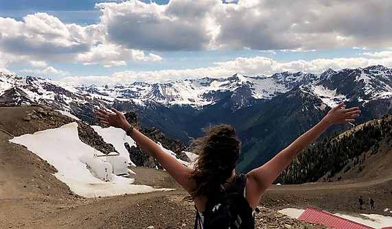 Woman with back to the camera and arms outstretched gazing upon snow capped mountains in the distance. Global Work and Travel Co - Tyla Working Holiday