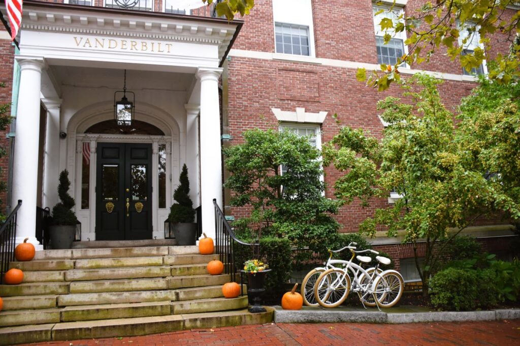 Front entry of the red brick Vanderbilt Hotel in Newport, Rhode Island. Steps lead to a beautiful portico over a grand set of black doors. Pumpkins  sit on each step and two bicycles are next to the entrance.