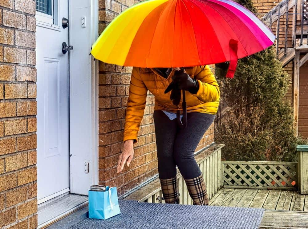Woman with umbrella leaving a gift bag on a doorstep