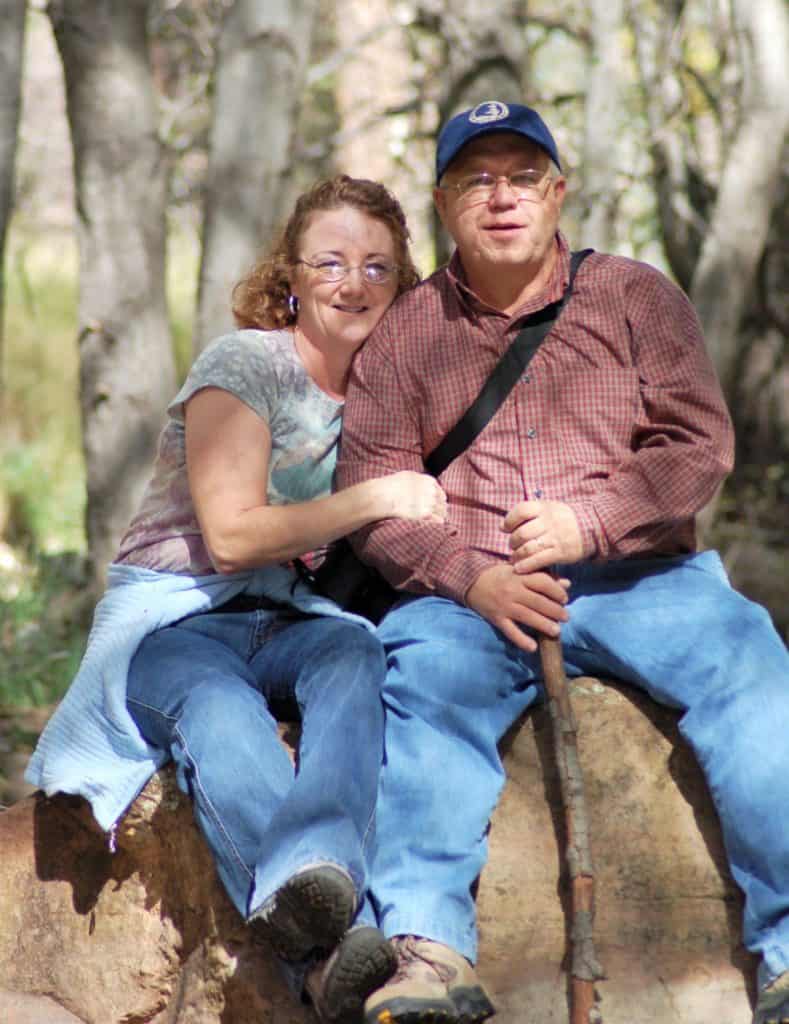 Man and woman sitting on a rock with trees in the background