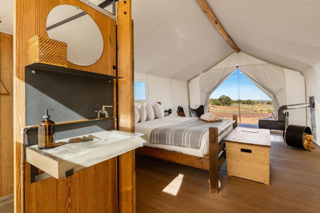 "Luxury glamping tent at Under Canvas in northern Arizona, near the Grand Canyon featuring a cozy bed, wooden floor and furnishings, and a rustic sink, with an open view of the scenic desert landscape through the tent's entryway."