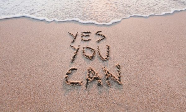 A sandy beach with the words "Yes you can" carved into the wet sand. Travel inspiration