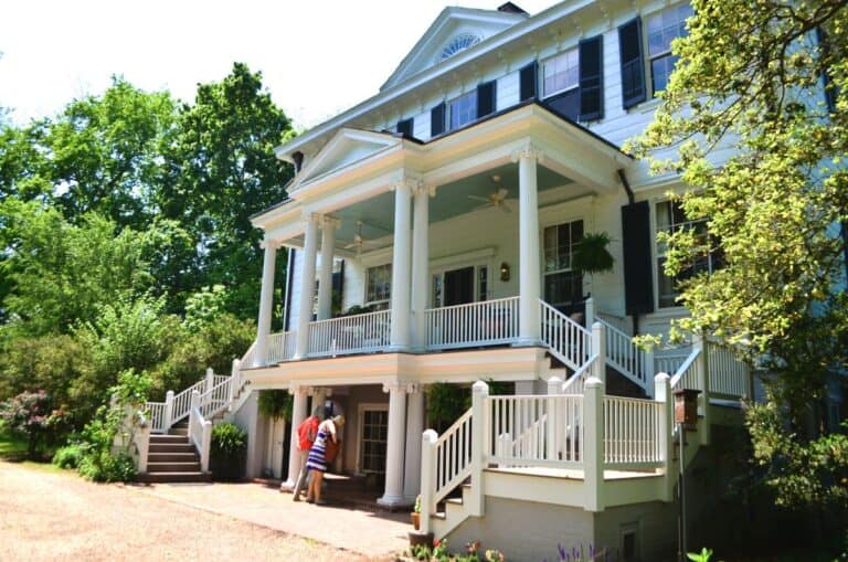 Two people peek inside a beautiful white 2 story Southern mansion with a 2-story front porch while on a Historic Garden Week of Virginia tour.