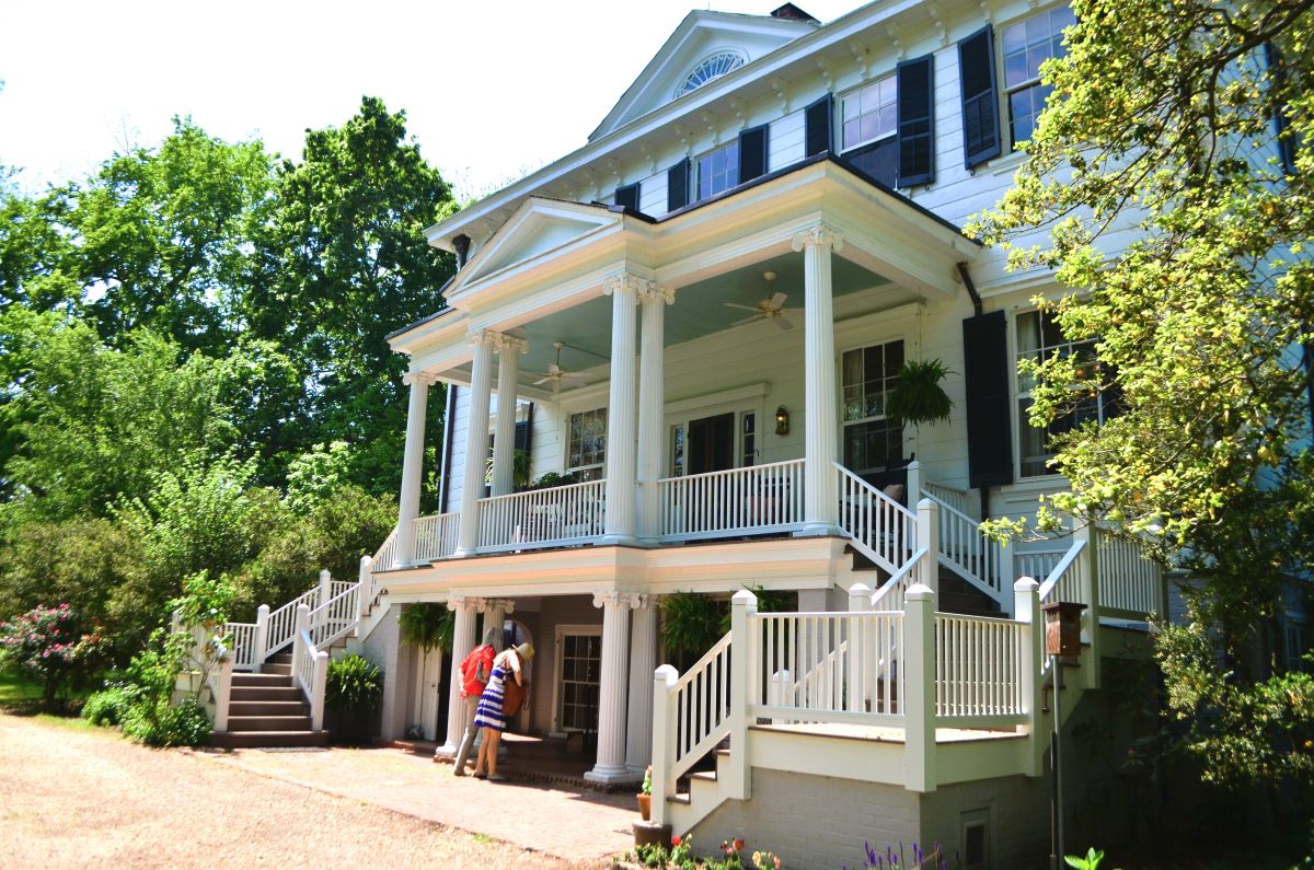 Two people peek inside a beautiful white 2 story Southern mansion with a 2-story front porch while on a Historic Garden Week of Virginia tour.