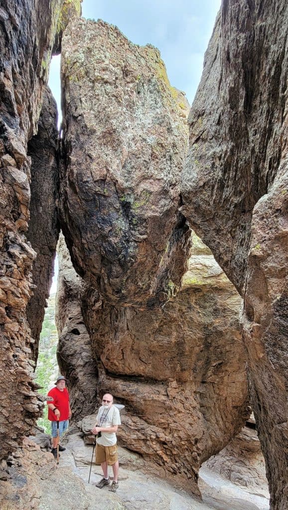 Massive boulder pinned between two rock formations hangs above 2 hikers in the Grottoes at Chiricahua National Park