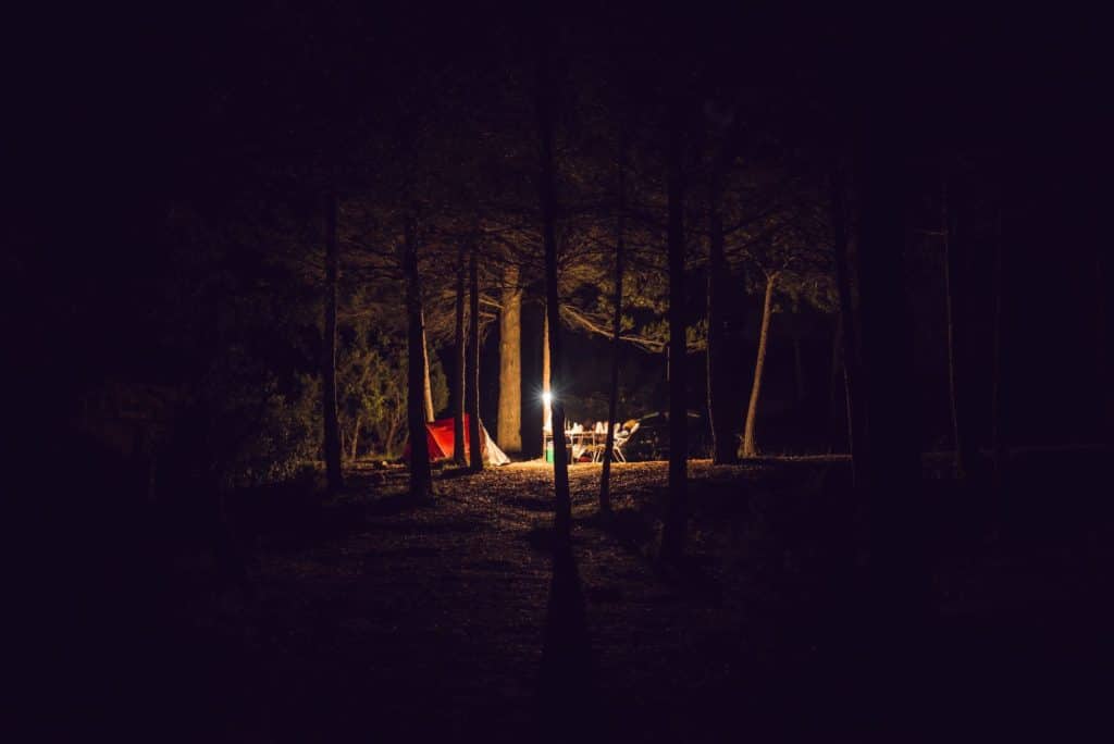 Red tent, camping chairs and table among the trees at night in an Arizona national park