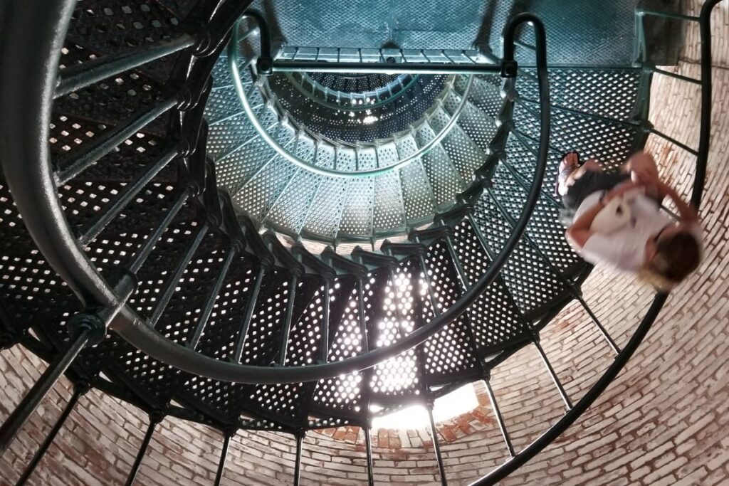 A woman walks down a black wrought iron spiral staircase inside the brick Currituck Beach Lighthouse in Corolla, North Carolina