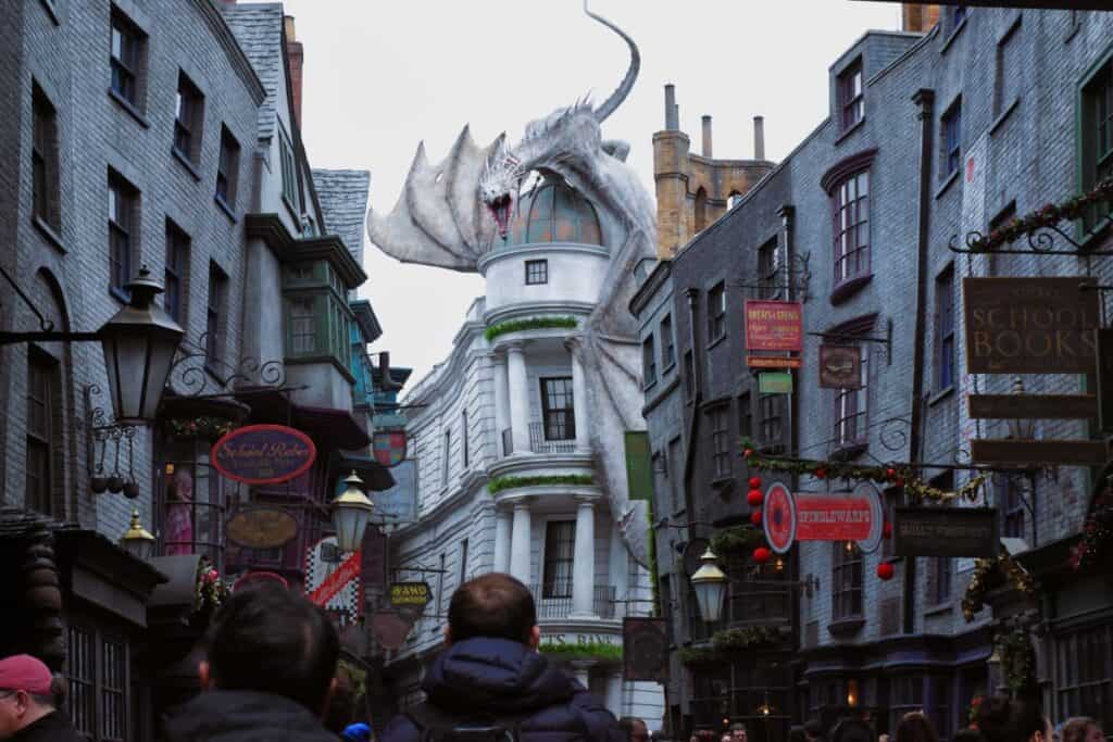 Universal Studios - A narrow street lined with crooked buildings and people looking up at a dragon perched on the roof of a building.