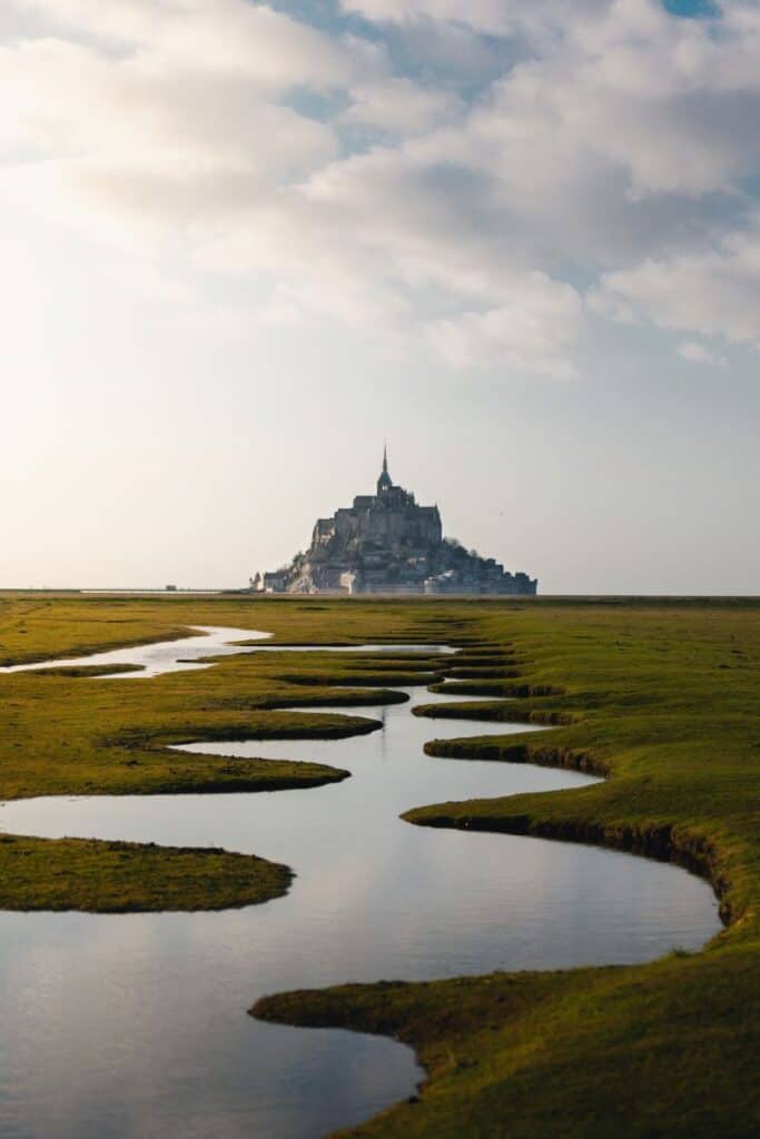 An ancient monastery built on an island in the Atlantic Ocean. A curvy river is in the foreground leading to Mont St. Michel in France. 