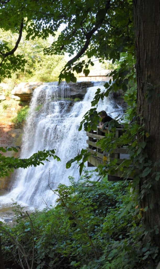Beautiful waterfall surround by green plants and trees. A person stands on a wooden platform looking at the falls. Cuyahoga Valley National Park, Ohio