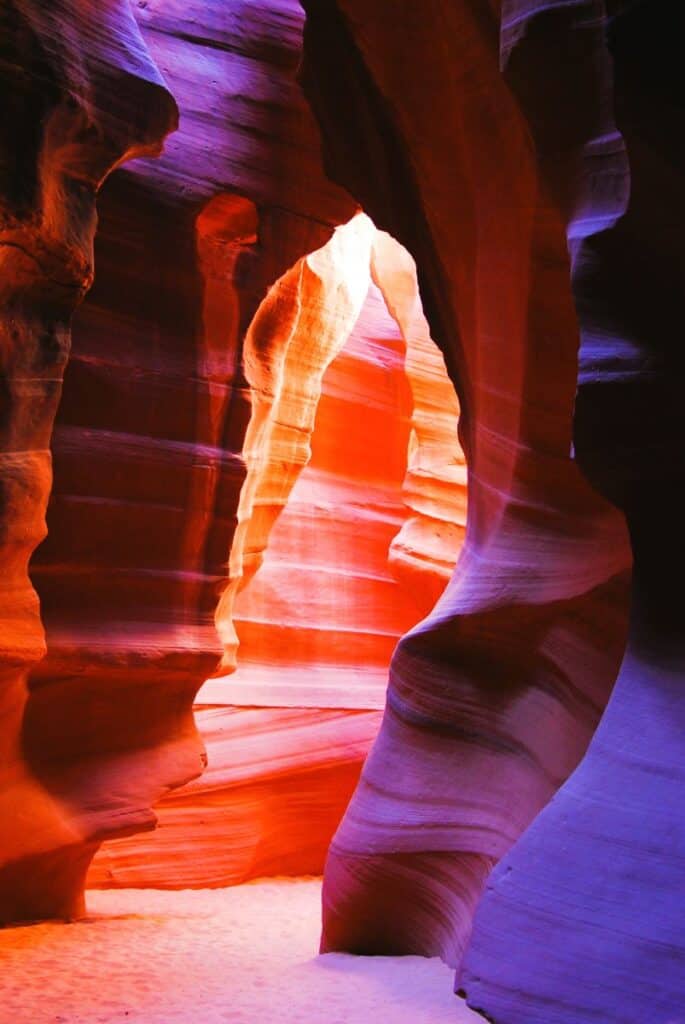 Many shades of orange, red and purple sandstone make up the walls of this beautiful slot canyon. Sunlight streams in from above and the floor is pale orange sand. Antelope Canyon Arizona