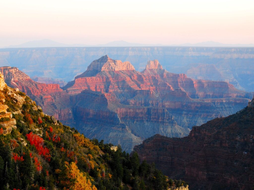 The North Rim of the Grand Canyon at sunset. Shades of orange, red and blue on the rock formations.