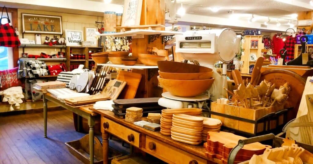 Inside a shop in Stowe Vermont. Wooden tables hold cooking supplies made of local wood, cutting boards, and the wall holds flannel blankets and fun signage.
