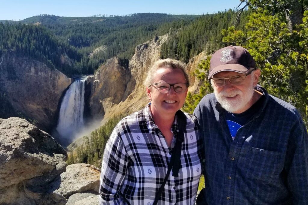 Man and woman wearing glasses stand at an overlook with Yellowstone Upper Waterfall in the background at Yellowstone National Park. Wyoming - Western States USA