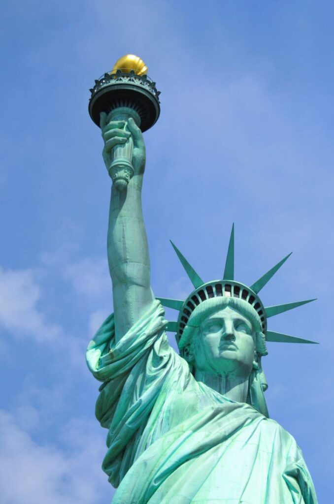 Close view of the Statue of Liberty from the waist up. You can see her head, her crown and her right arm lifting the gold torch above her head. New York City, NY - Northeast region of the USA