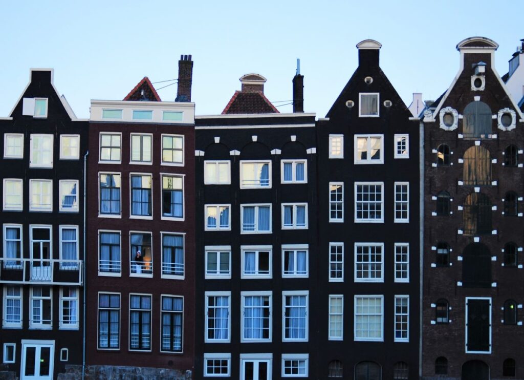 A woman stands in the window of a building in a row of classic black Dutch gabled houses in Amsterdam showcases the city's charming architecture and vibrant culture, making it a must-see destination for anyone exploring travel in Europe.