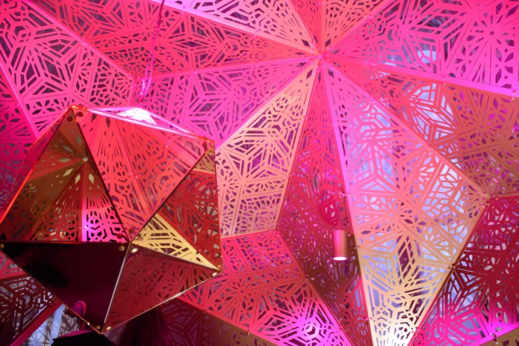 Bright pink lighting illuminates a metal sculpture with intricate patterns by HYBYCOZO at the Renwick Gallery in Washington DC. 