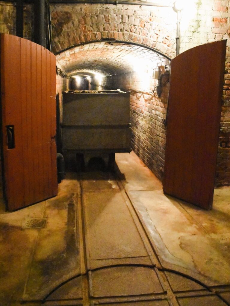 Two wooden doors stand open revealing a brick-walled tunnel and a small coal cart on railroad tracks in the basement of the Elms Mansion, Newport, Rhode Island