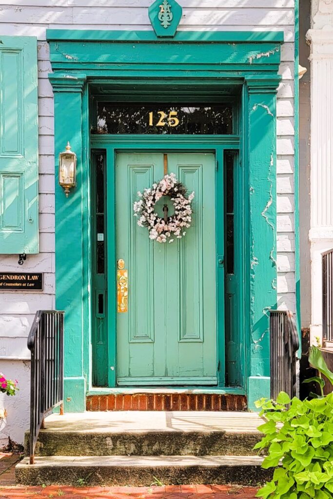 Aqua colored front door on a historical home with ornate trip and decorations. A brick steps lead to the door and a wreath of cotton hangs on the door in Harrisburg, Pennsylvania