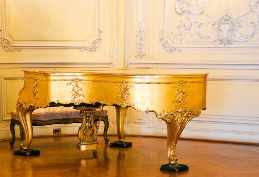 Newport Mansions - A golden grand piano sits in a room with a wood floor and intricately decorated walls at the Elms Mansion, Newport, Rhode Island