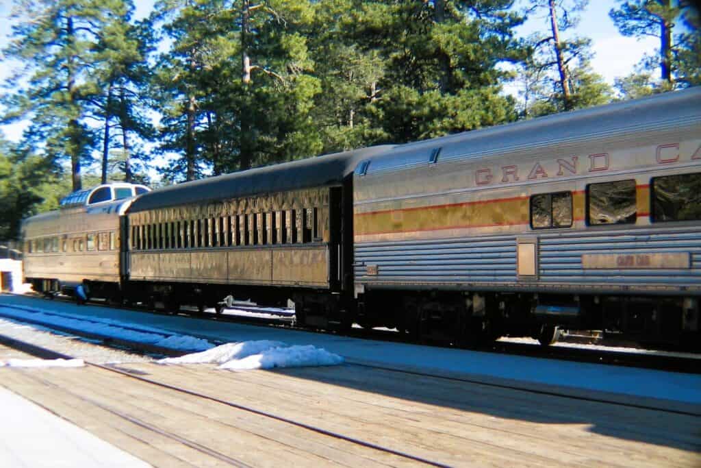 3 railroad cars sit on the tracks of the Grand Canyon Railroad. This train takes people from Williams AZ to the South Rim of the Grand Canyon. Small patches of snow are on the ground.
