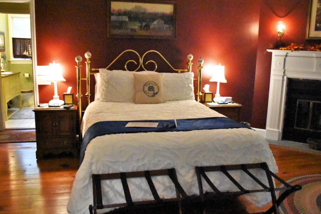 Hyde Park vacation rental in Hudson Valley NY - beautiful queen size bed with a brass headboard. The walls are painted deep red and there is a fireplace to the right of the bed. The floors are wood and there's a glimpse of the bathroom through the door.