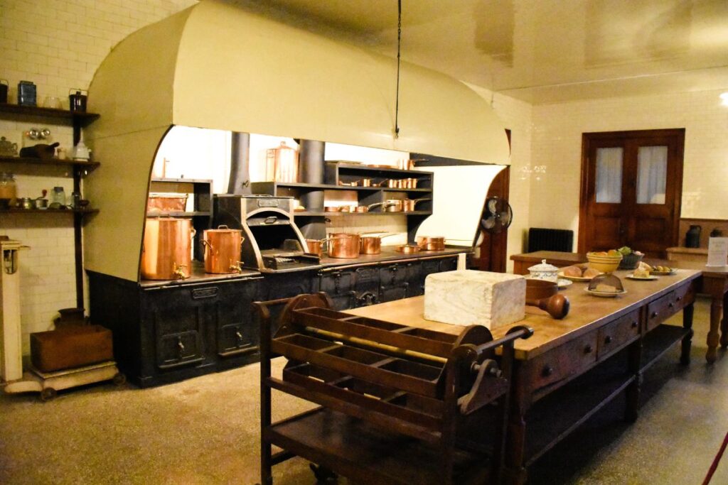 Historic kitchen from the Gilded Age in Newport, Rhode Island, USA. This kitchen is at The Elms mansion in the basement.  A long wooden table holds various kitchen items and a huge cast iron stove and oven lines the back wall of the room.