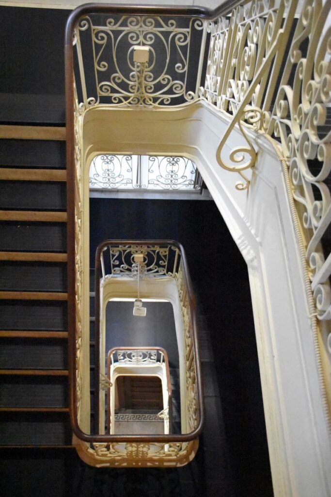 The servants' back staircase at the Elms Gilded Age mansion in Newport, RI. Several levels of stairs with white decorative wrought iron railings. 