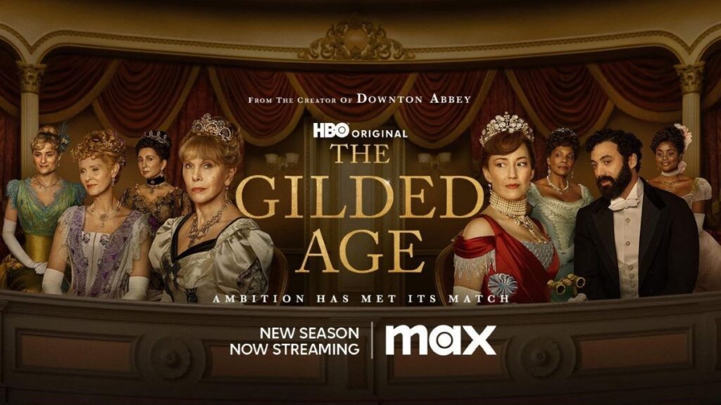 Seven formally dressed  women and one man sit in a fancy theatre box. They're dressed in costumes and tiaras from the Gilded Age. Text says "From the creators of Downton Abbey, HBO original, The Gilded Age. Ambition has met its match. New season now streaming on Max."