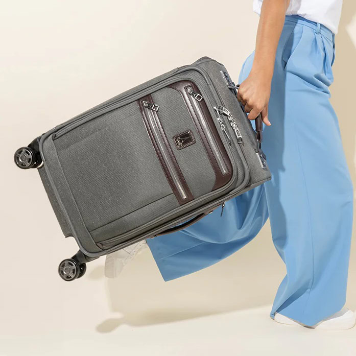 Woman wearing blue pants is walking with a piece of gray carry-on size Travelpro luggage in her hand.