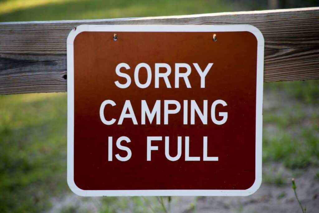 Brown sign with white lettering hangs on a board. Text says "Sorry camping is full"