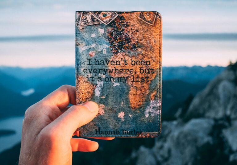 Person holding a small leather bound book with a map in the background of the book cover and the words "I haven't been everywhere, but it's on my list."