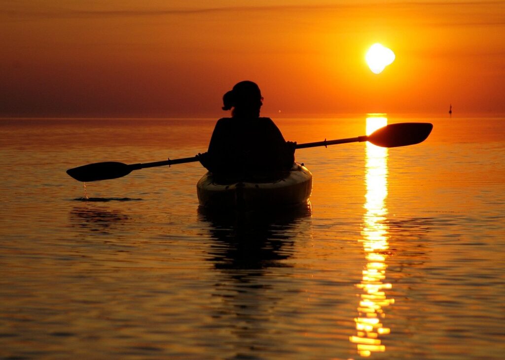 Kayaker paddling at sunset on a Cape Hatteras wildlife viewing kayak tour, with golden light reflecting on calm Outer Banks waters.